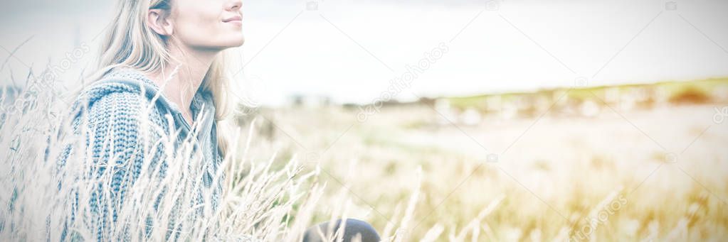 Side view of a cute thoughtful young woman sitting on grass at beach