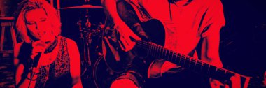 Gece kulübünde sahnede dijital tablet tutan gitarist genç kadın şarkıcı