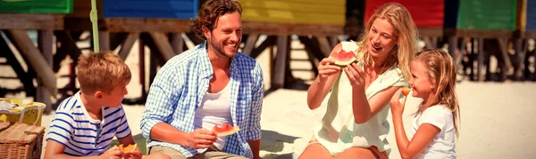 日当たりの良い日中にビーチで毛布に一緒に座ってスイカを食べて幸せな家族 — ストック写真