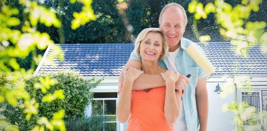 Happy older couple holding paint roller against pretty house with a blue and white filter clipart
