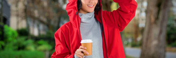 Kobieta Czerwonej Kurtce Kawie Białym Tle Przeciwko Chodnik Przez Drzewa — Zdjęcie stockowe