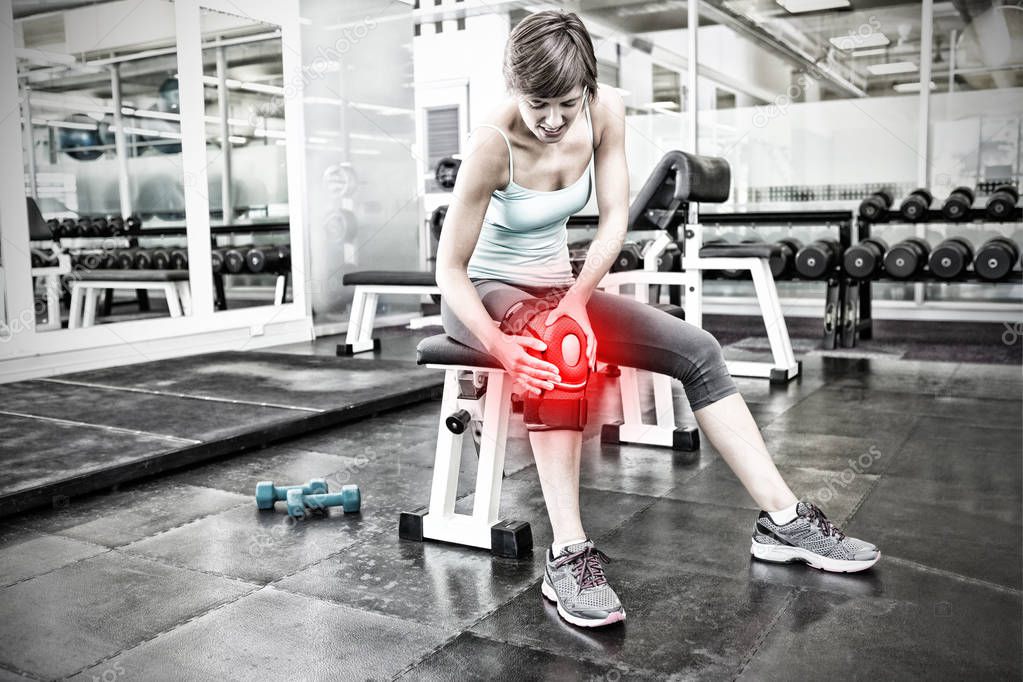 Fit brunette sitting on bench holding injured knee against highlighted pain