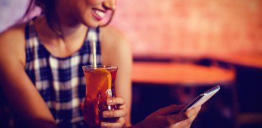 Barda kokteyl içki yaparken cep telefonu kullanan genç kadın
