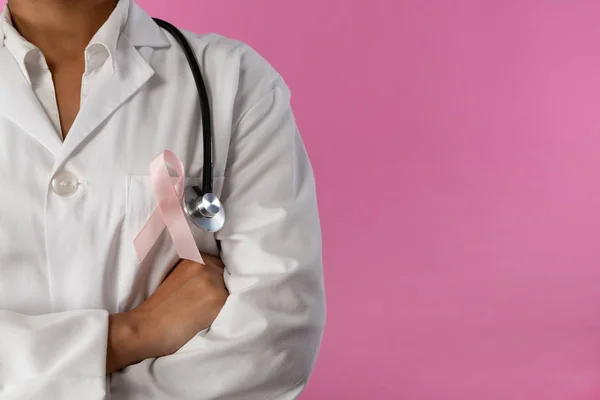 手臂交叉护士戴着乳癌意识粉红丝带粉红色的背景 关闭粉红色丝带 — 图库照片