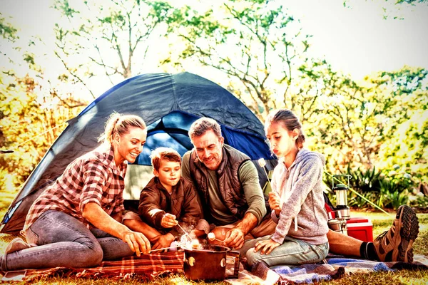 Family roasting marshmallows outside the tent on a sunny day