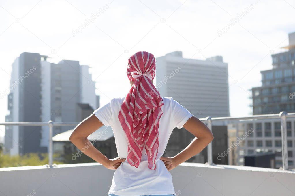 Confident woman standing in city for breast cancer awareness against urban background