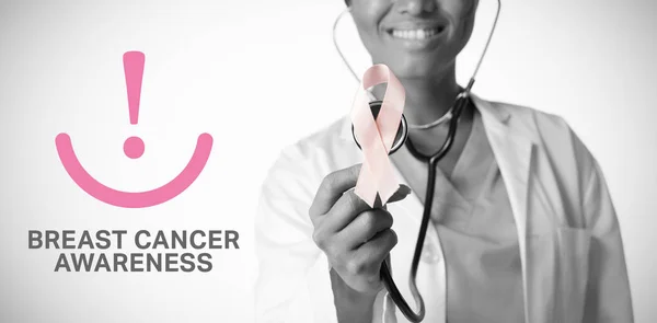 ピンクのリボンと聴診器を保持している女性医師に対して乳房がん啓発メッセージ — ストック写真