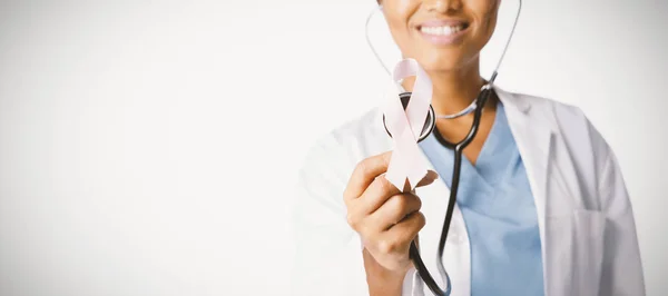 白地にピンクのリボンと聴診器を保持している女性医師 — ストック写真