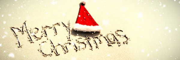 サンタの帽子が付いている砂に書かれたメリー クリスマスに対して雪 — ストック写真