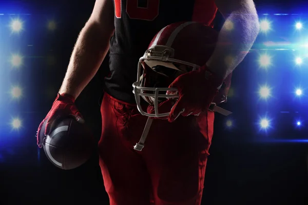 ヘルメットとラグビー ボールを持って立っているアメリカン フットボール プレーヤーの中央部 — ストック写真