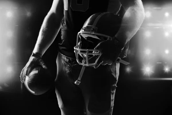 美国足球运动员带着头盔和橄榄球站着的中段 — 图库照片