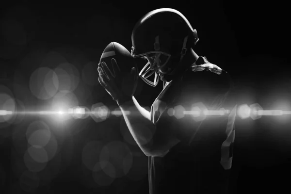 美国足球运动员拿着橄榄球头盔和球站着的侧视图 — 图库照片