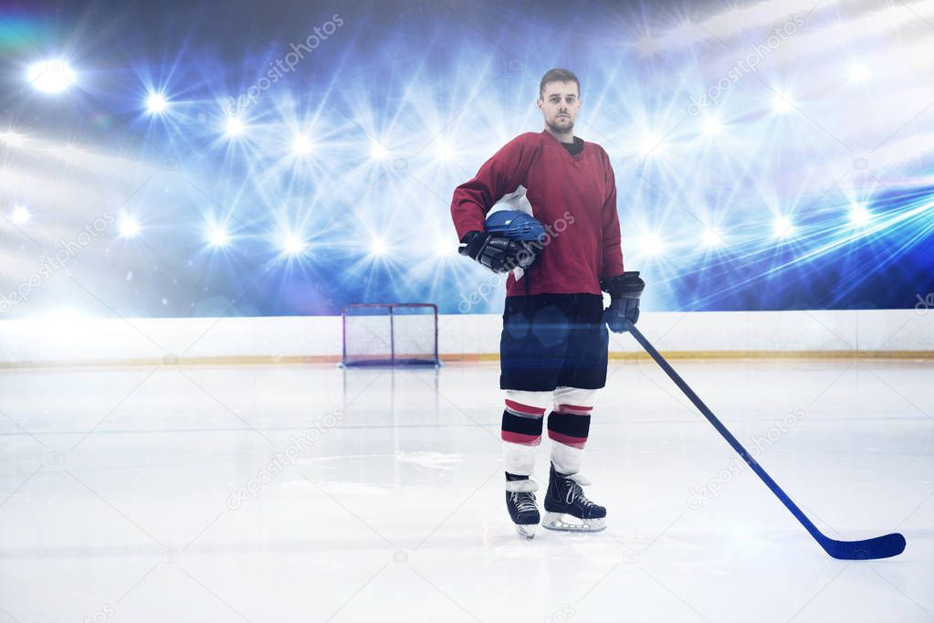 Portrait of ice hockey player holding helmet and stick against view of strong lights