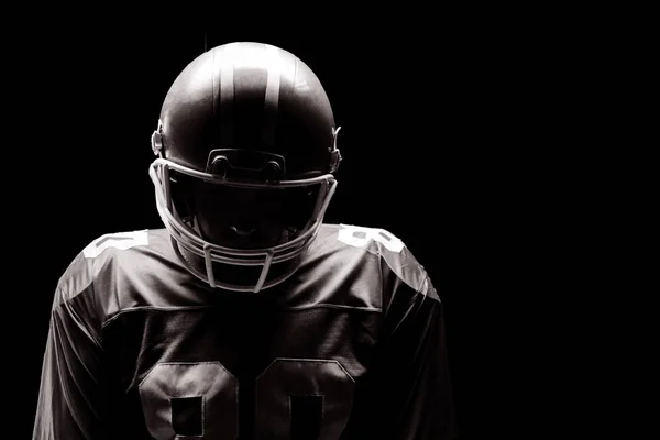 黒の背景にラグビー ヘルメットと立っているアメリカン フットボール プレーヤー — ストック写真