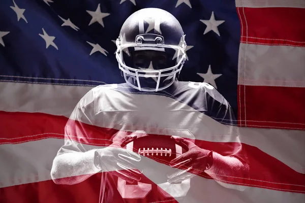 美国红白相间的国旗特写镜头反对拿着橄榄球头盔和球站着的美国足球运动员 — 图库照片