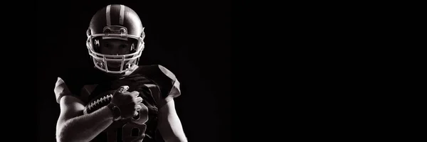 黒の背景にラグビー ボールを保持しているヘルメットのアメリカン フットボール プレーヤー — ストック写真