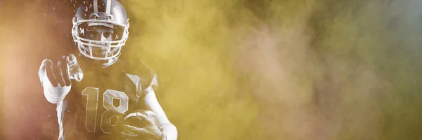 Разбрызгивание Пыли Американского Футболиста Шлеме Держащего Регбийный Мяч Указывающего — стоковое фото