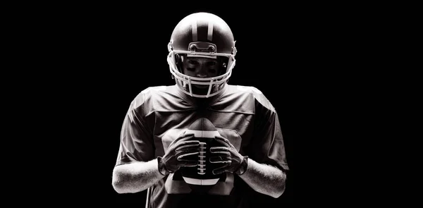 ラグビー ヘルメットとボール黒の背景に立っているアメリカン フットボール プレーヤー — ストック写真