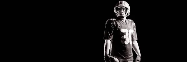 美国足球运动员站在黑色背景下拿着橄榄球和头盔 — 图库照片