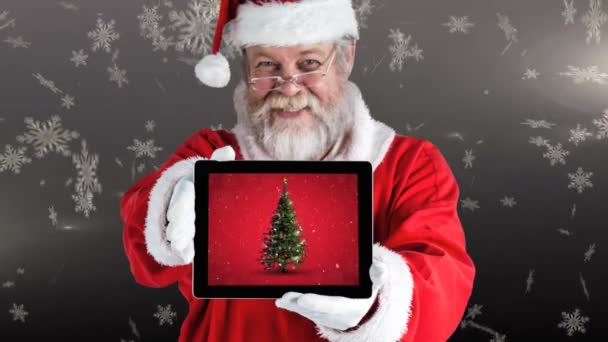 圣诞节动画快乐的圣诞老人拿着一个数字平板电脑 显示圣诞树 雪花落在灰色的背景4K — 图库视频影像