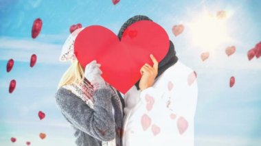 Çift yüzlerini önünde büyük kırmızı kalp kalp balon gökyüzüne doğru yüzen güneşli günde tutan kış kıyafetleri