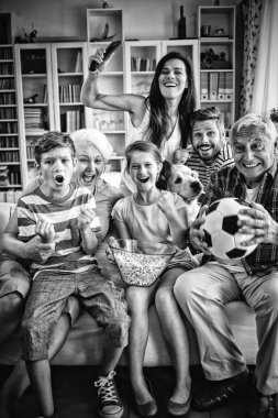 Happy multi-generation family watching soccer match on television in living room at home clipart