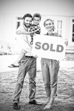 Portrait of happy family standing outside home with sold sign clipart