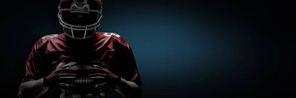 美国足球运动员站在橄榄球头盔上 拿着橄榄球在蓝色背景下 带着小插曲 — 图库照片