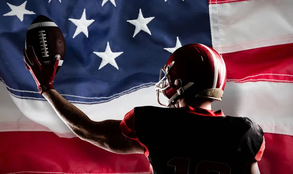 美国足球运动员戴头盔拿着橄榄球 对抗全框架的美国国旗 — 图库照片