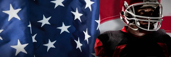 アメリカの国旗のクローズ アップに対するラグビー ヘルメットに立っているアメリカン フットボール プレーヤー — ストック写真