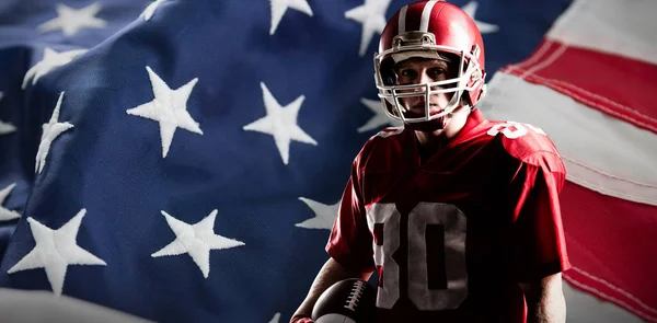 美国足球运动员戴头盔拿着橄榄球 对抗全框架的美国国旗 — 图库照片