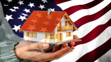 Küçük oyuncak ev animasyonlu Amerikan bayrağı arka planda tutan kadın