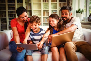 Neşeli aile evde kanepede otururken teknolojilerini kullanarak