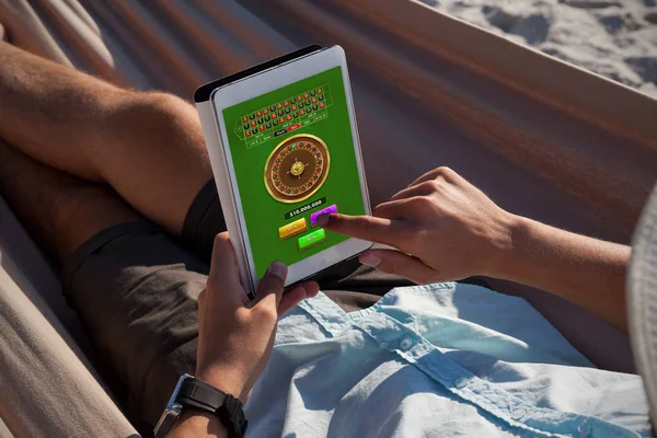 ハンモックでリラックスしたり ビーチでデジタル タブレットを使用して男に対してオンライン ルーレット ゲーム — ストック写真