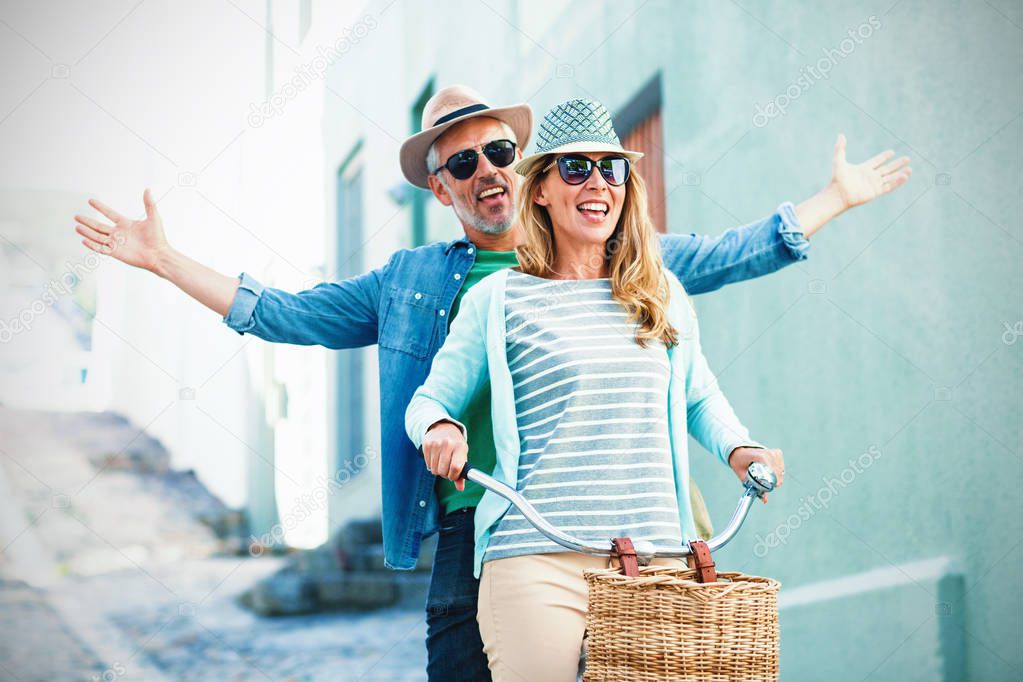 Mature couple enjoying while riding bicycle by building