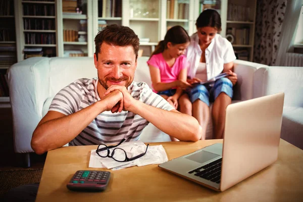 Smiling Man Sitting Table Bills Laptop While His Wife Daughter — Φωτογραφία Αρχείου