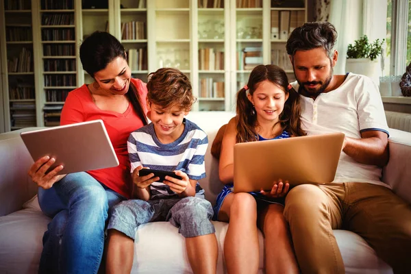 Família Usando Várias Tecnologias Enquanto Senta Sofá Casa — Fotografia de Stock