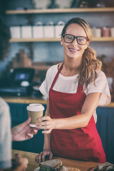 Portrait of waitress serving a coffee to customer at counter in cafe 