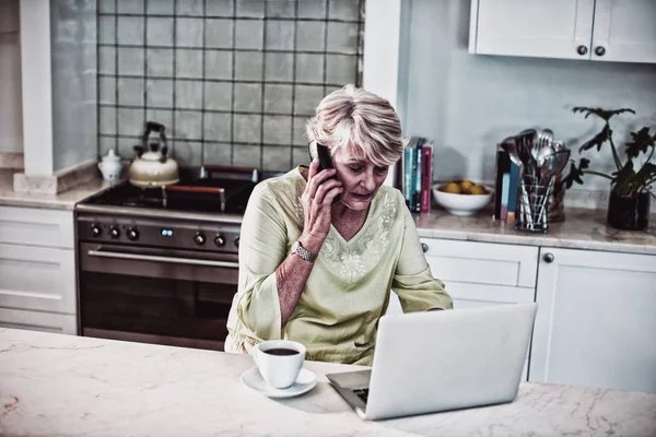 Старшая Женщина Разговаривает Мобильному Телефону Время Использования Ноутбука Кухне — стоковое фото