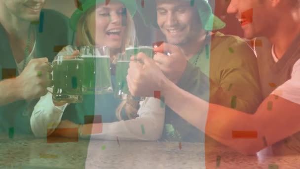 年轻的多样化的人拿着绿色啤酒 为圣帕特里克节敬酒 背景上飘扬着爱尔兰国旗 五彩纸屑落在前景上 — 图库视频影像