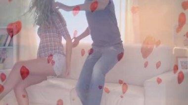 Dijital arkaplanda uçan dijital kalplerle kanepede zıplayan beyaz bir çiftin dijital kompozitosu.