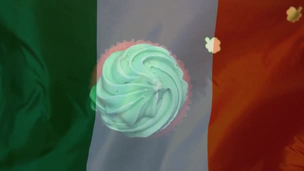稿では緑の背景に手を振るアイルランド国旗に対するアイシングでカップケーキに落ちて少し Shamrocks のデジタル合成 — ストック動画