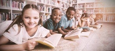 İlkokulda kütüphanede kitap okuyarak yerde yatan gülümseyen okul çocukları