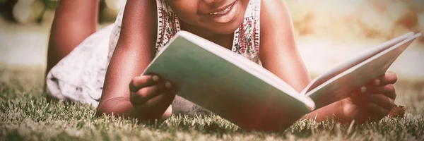 读一本书躺在公园的小女孩 — 图库照片