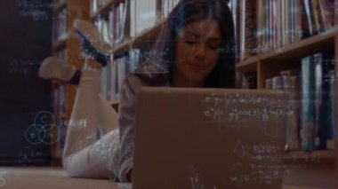Mutlu karışık yarış kız öğrencinin matematik sembolleri tarafından çevrili kitaplığındaki yalan onu laptop kullanarak dijital bileşik