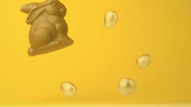 Paskalya yumurtaları ile çikolata Paskalya tavşanı Dijital kompozit düşer ve sıçrar. Sarı turuncu arka plan.