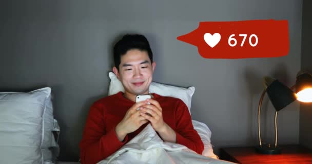 一个亚洲男子躺在床上检查手机的正面景色 在他旁边的前景是一个数字动画的消息气泡与心脏图标增加计数4K — 图库视频影像