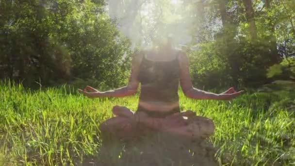 草の上に座って森の中で瞑想している女性の正面図 彼女の後ろには木がある — ストック動画