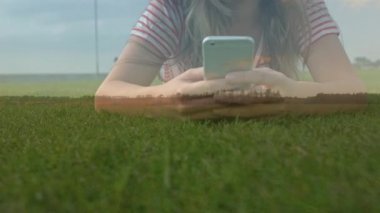 Telefonuna mesaj atarken çimenlerin üzerinde yatan bir kadının yakınçekimini