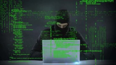 Bir dizüstü bilgisayar ve ön planda kullanırken sağa ve sola bakan kafkas bir hacker dijital kompozit program kodları gösterir.